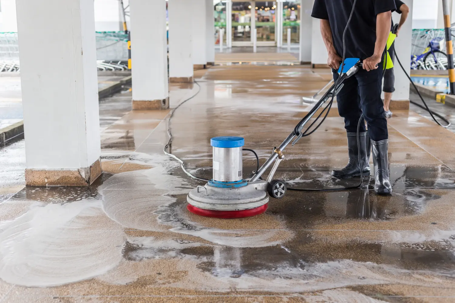 Arbeiter reinigt Sand und wäscht Außengehweg mit Poliermaschine und Chemikalien oder Säure