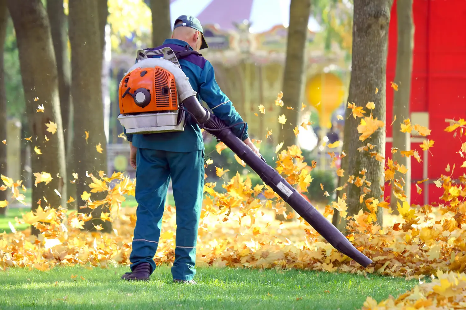 Arbeiter im Park reinigen das Gras mit Hilfe einer Windkraftanlage von abgefallenen Blättern